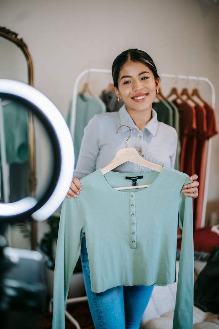 Smiling young woman showcasing clothing item during a fashion vlog at home.